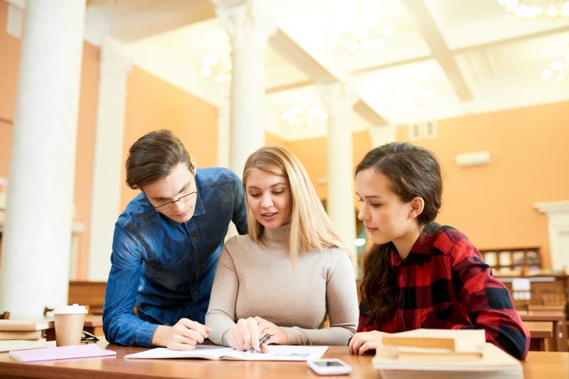 Three students sitting and reading catalog in library