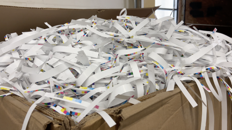 Scraps of paper from various print projects sit in a cardboard box waiting to be recycled.